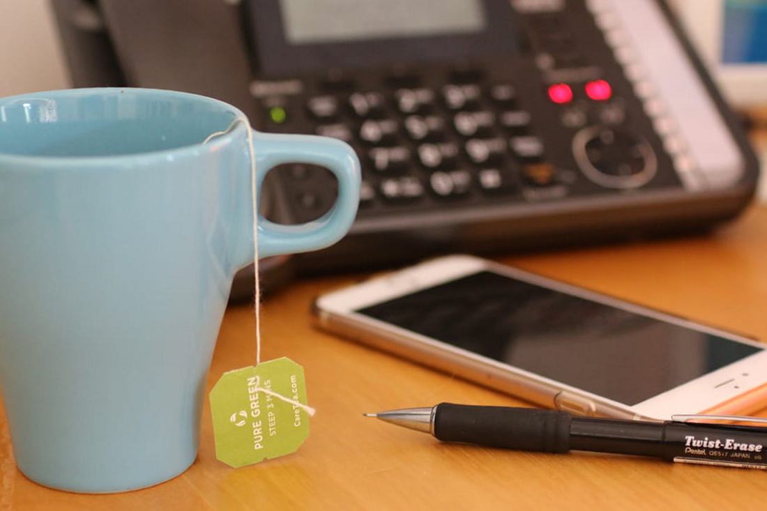 A desk with a coffee cup, notebook and telephone